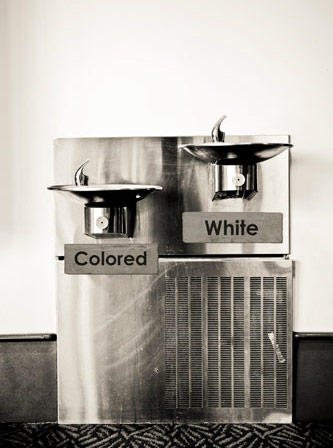 Image of drinking fountains marked “colored” and “white” indicating racism and discrimination