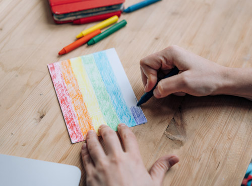 Man colors a rainbow index card on a wood table for display in his office.