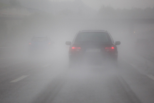 Car with red brake lights driving through a dense fog, illustrating how depression can result in cognitive dysfunction.