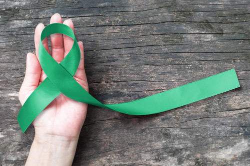 hand holding a green ribbon, the symbol for mental health month