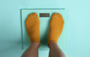 Stocking feet standing on a scale on a teal blue background, signifying concern than antidepressant may cause weight gain
