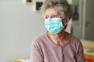 Gray haired older woman wearing a protective face mask who may be suffering from geriatric depression