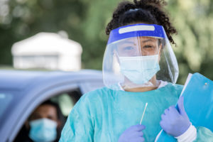 Female, Hispanic burnout healthcare professional preparing to give COVID test at drive-through test site.