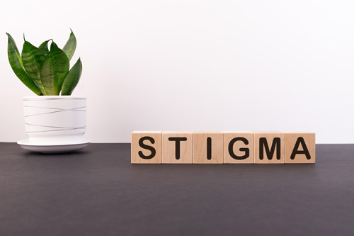 The word stigma written on blocks of wood in front of light background and a plant referring to minority mental health issues. .