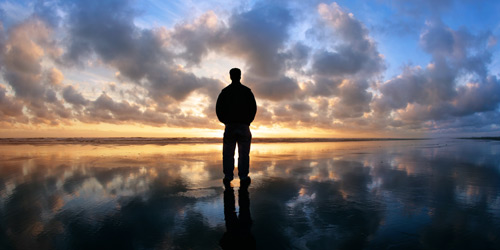 Silhouette of a man looking out at a sunset over a beach, like a person emerging from depression.