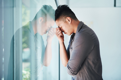Asian man suffering from depression leaning against glass 