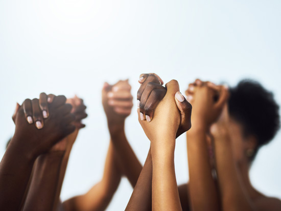 Black women clasp hands and hold them in the air indicating solidarity against the stigma of minority mental health.