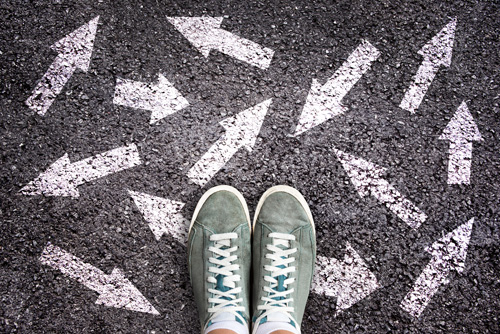 Teenager in cool shoes stands on pavement painted with white arrows pointing in different directions.