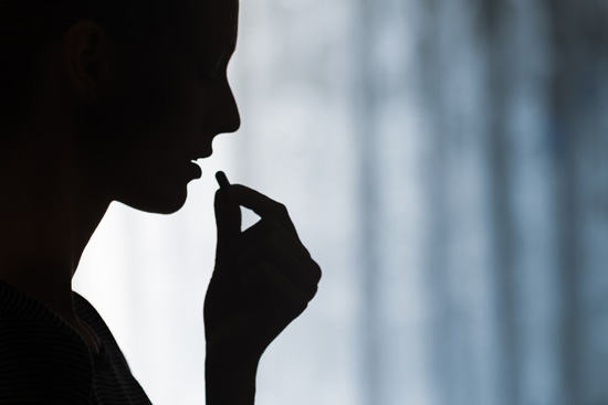 Silhouette of a woman against a white curtain taking an antidepressant.