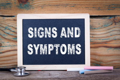 Black chalk board with white letters that say “SIGNS AND SYMPTOMS” showing the importance of recognizing signs of anxiety.