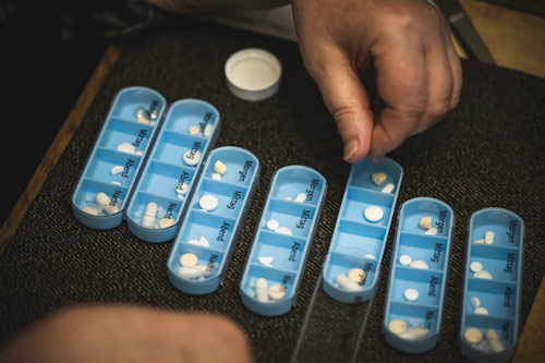 Senior man puts pills into a 7-day blue pill organizer to manage multiple medications in depression treatment.