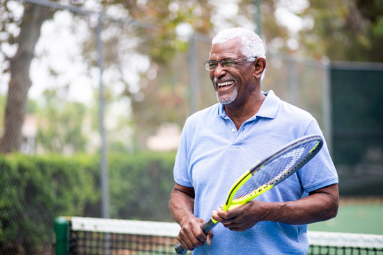 Senior black man playing tennis, illustrating importance of staying active as we age, especially if battling depression.