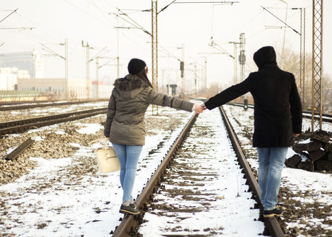 Couple holding hands walking on railroad tracks in the snow, helping with their anxiety or depression