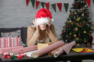 Depressed frustrated woman wrapping Christmas gift boxes, representing holiday stress 