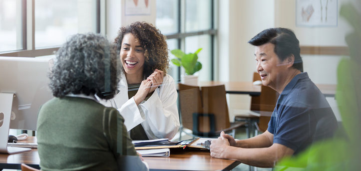 Adult female mental healthcare provider or psychiatrist clasps her hands happily with news for adult couple.
