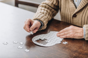 Senior man with Alzheimer’s put together white puzzle of human head, showing necessity to check for depression.