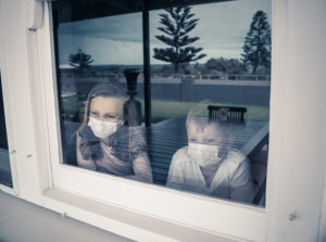 Children wearing masks looking out the window appearing depressed due to COVID.