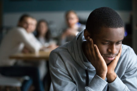 Young African American male sitting alone and feeling judged by others in the room