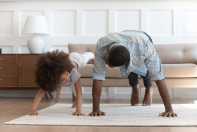 Black man doing yoga with young daughter, showing importance of reaching out when needing mental health help.