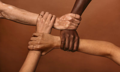 4 multicultural men grasps each other’s wrists forming a square, showing how supporting each other through mental health challenges may help. 