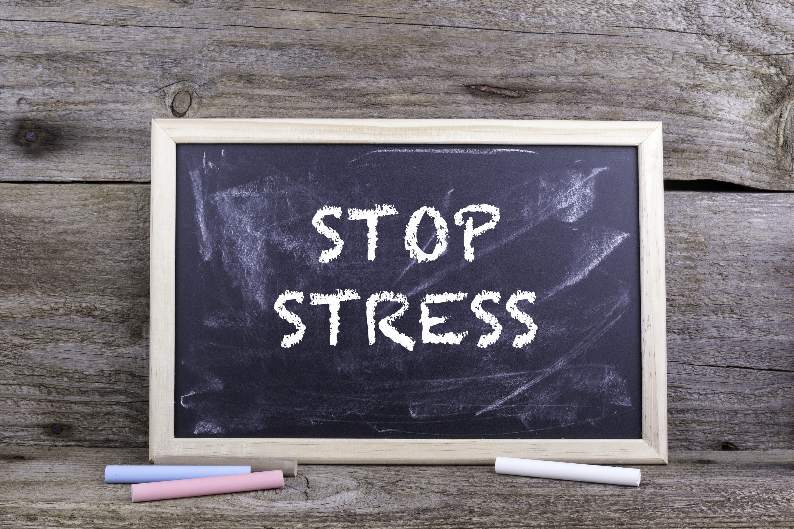 Old wooden background with texture with a chalk blackboard that says “Stop Stress.”
