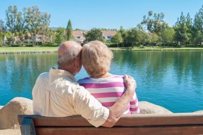 Senior couple looks out at lake on sunny day, reinforcing the question of retiring to a sunny place will stave off depression