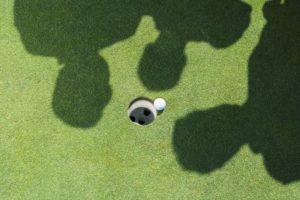 Shadows of golfers over golf ball next to hole, showing how retirement may lead to depression