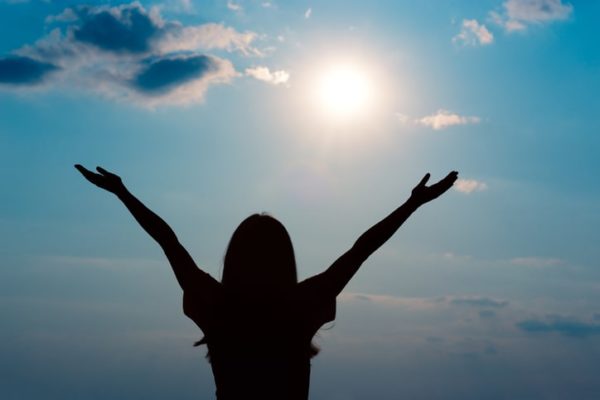 Woman raising arms looking at the sun, illustrating studies are inconclusive on Vitamin D and depression.