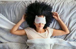 Black woman asleep in bed with cat-theme sleeping mask over her eyes showing depression treatment may lead to better sleep.
