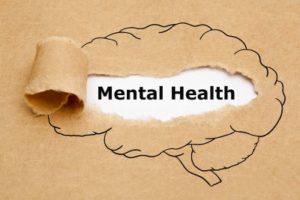 Brown piece of paper torn, showing the words "mental health" written on white paper underneath.
