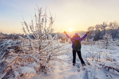 Hiker raising arms to winter sun in snow-covered forest, showing how to cope with seasonal affective disorder (SAD)
