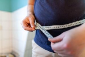 Man using tape to measure abdomen showing concern of antidepressants and weight gain