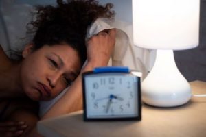 Black woman looks exhaustedly at an alarm clock showing 3:35, demonstrating potential depression or sleep disorder.