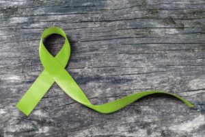 Green ribbon against weathered wood plank, illustrating concept of mental health stigma-free campaign
