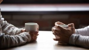 Close up woman and man holding cups of coffee on table, discussing mental health while dating