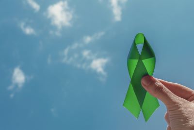 Man's hand holding green ribbon against blue sky signifying fight against mental health stigma