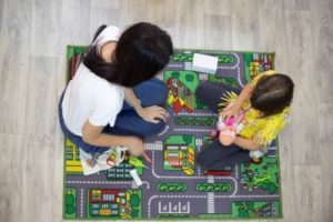 Mental health therapist sits with young child on colorful rug talking about depression symptoms