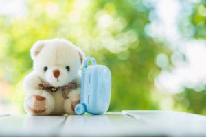 Teddy bear sitting on wooden table with blue luggage, showing importance of talking to young children about mental health