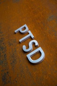 The word PTSD laid with silver metal letters on flat rusted steel sheet background showing how trauma-induced depression impacts people.