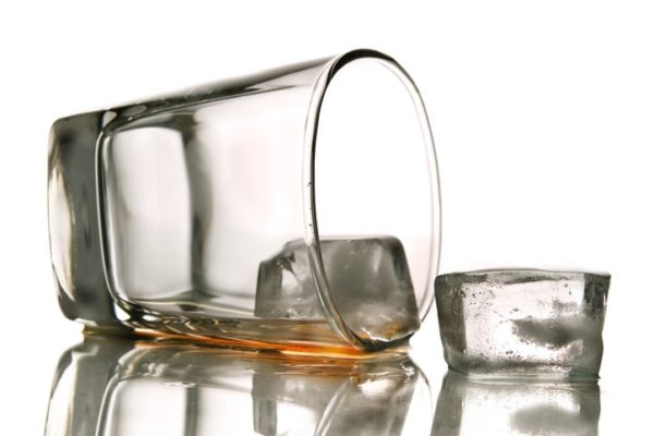 Empty brandy tumbler on side spilling drink and ice cubes, illustrating link between depression and substance abuse