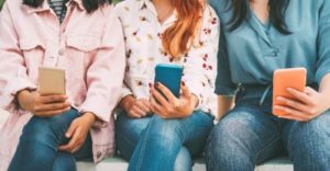 Teenagers all checking their mobile devices to illustrate correlation between popularity and good mental health
