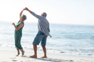 Senior couple dances on the beach reinforcing how social connections are important in managing depressive symptoms