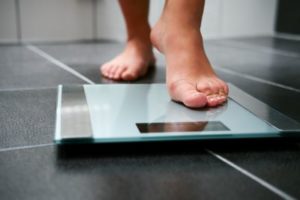 Female steps on scale against black tiled floor, demonstrating concern that depression could lead to weight gain.
