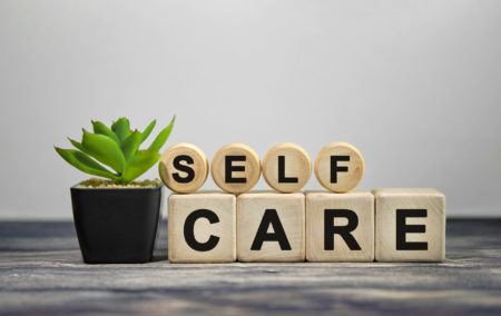 Self care text on wooden cubes with green plant in block pot, showing importance of self care in avoiding caregiver burnout