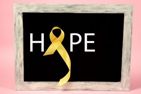 Yellow ribbon for suicide prevention awareness forms the “o” on a blackboard on which HOPE