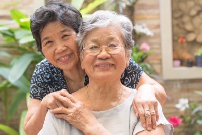Younger Asian woman caregiver hugging her older mother