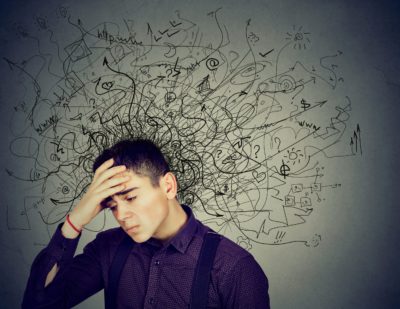 Young Latino man with hand to forehead surrounded by pencil drawings of squiggles indicating his ADHD