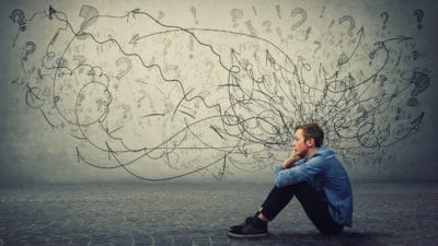 Young man looks pensive surrounded by pencil drawings of squiggles and questions marks demonstrating the difficulty of ADHD