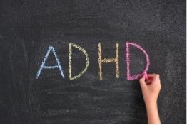 Child writes “ADHD” on blackboard in colorful chalk.