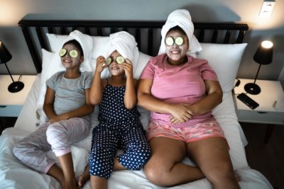 Black mother and daughters relieving stress with skin care routine and cucumber slices over the eyes.